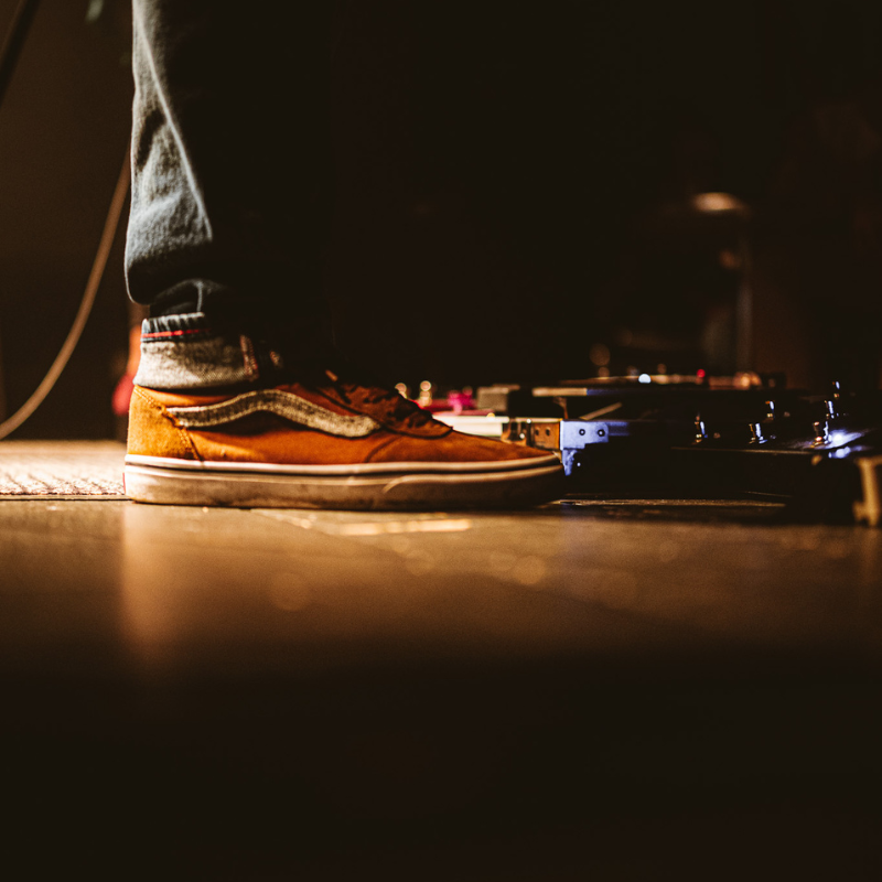 Gros plan sur le pied d’un musicien activant un pédalier d’effets de guitare en concert d’Ol’d Tam, duo Jukebox