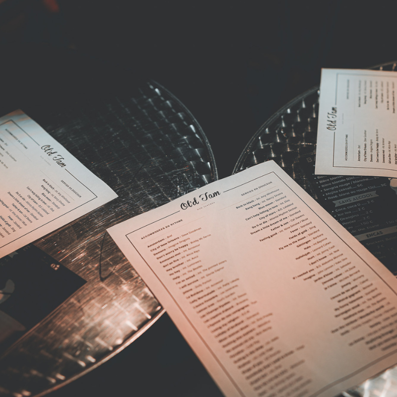 Menus des chansons d’Ol’d Tam posés sur une table, offrant plus de 80 titres variés au choix du public