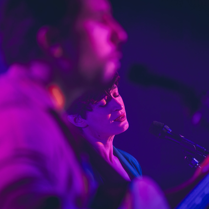 Tamara, chanteuse et bassiste d’Ol’d Tam, interprétant un titre les yeux fermés, dans une lumière violette