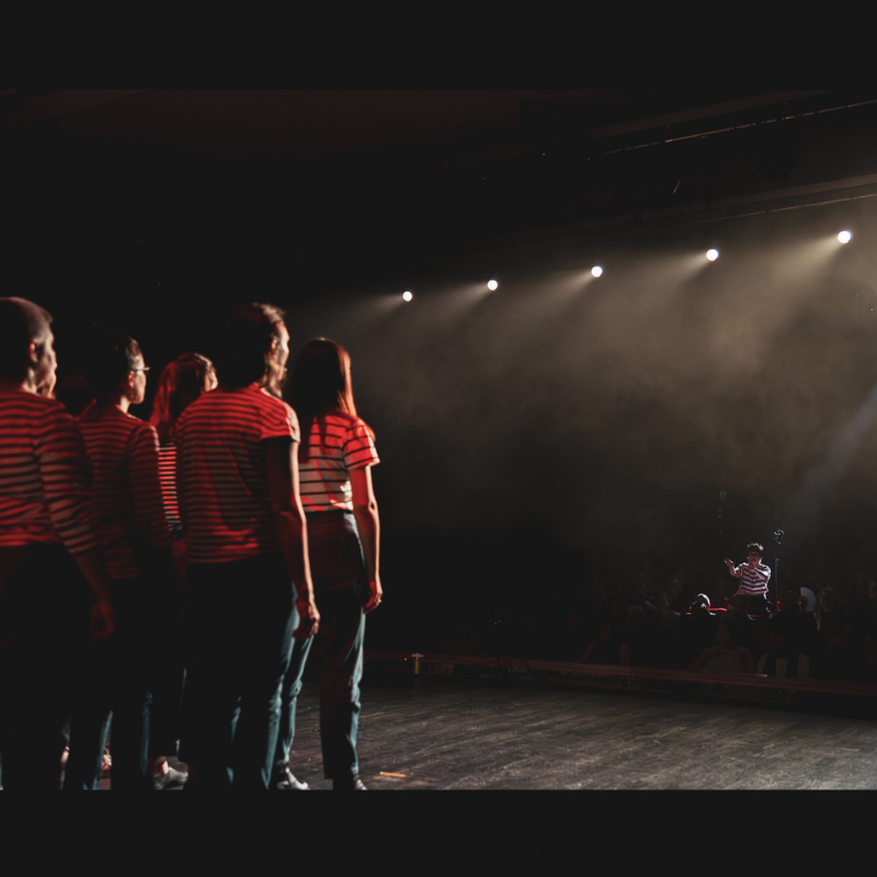 Choristes de la Chorale Pirate en concert a cappella, dirigés sur scène sous les projecteurs
