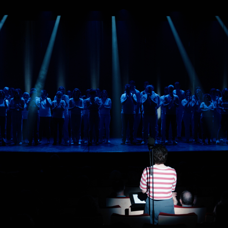 La cheffe de chœur de la Chorale Pirate dirige dans un éclairage bleu intense