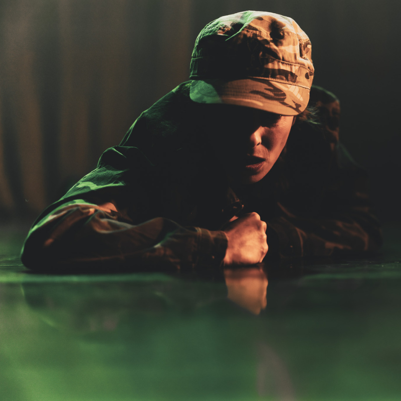 Interprète en uniforme militaire, allongée au sol dans une lumière verte dramatique du spectacle Splendeur & Décadence