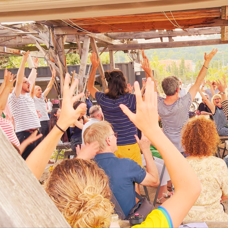 Public et chanteurs de la Chorale Pirate levant les bras ensemble dans une animation musicale.