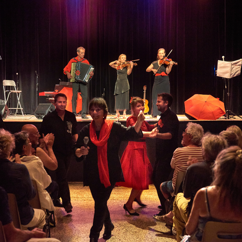 Plusieurs artistes dans la salle valsent avec le public tandis que d'autres restent sur le plateau pour jouer de la musique lors de la dernière chanson du spectacle "Chansons & Coquelicots", hommage à Anne Sylvestre.
