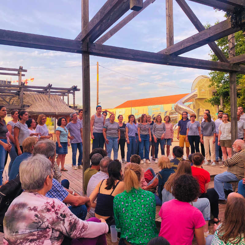 La Chorale Pirate chante devant un public en extérieur sous une structure en bois à la Station Mue, Lyon Perrache.
