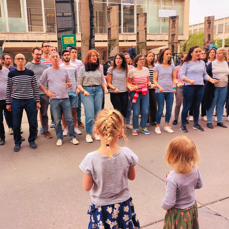 La Chorale Pirate chante en extérieur face à deux enfants spectateurs lors de la fête du livre jeunesse à Villeurbanne.