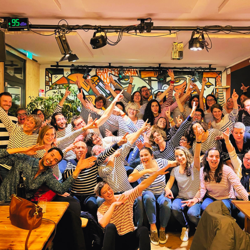 Tous les choristes de la Chorale Pirate réunis dans une salle, posant joyeusement pour une photo de groupe.
