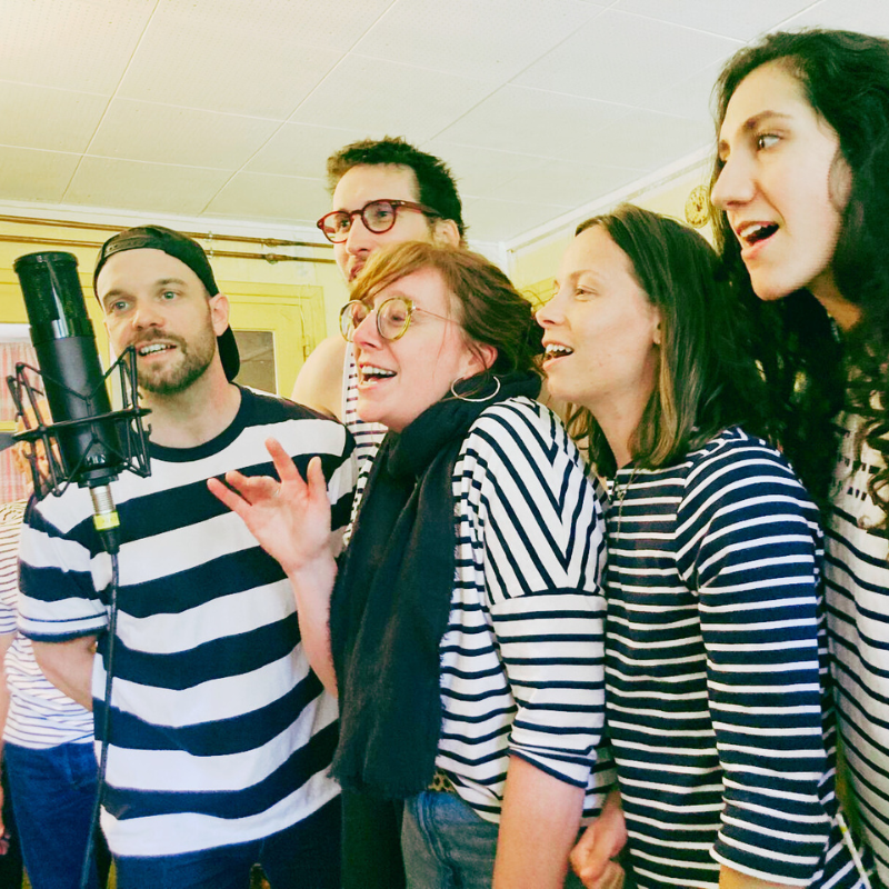 Plusieurs choristes de la Chorale Pirate réunis autour d’un micro pour un chant collectif.