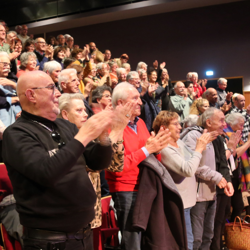 Spectateurs debout applaudissant chaleureusement à la fin du spectacle Chansons & Coquelicots, hommage à Anne Sylvestre.