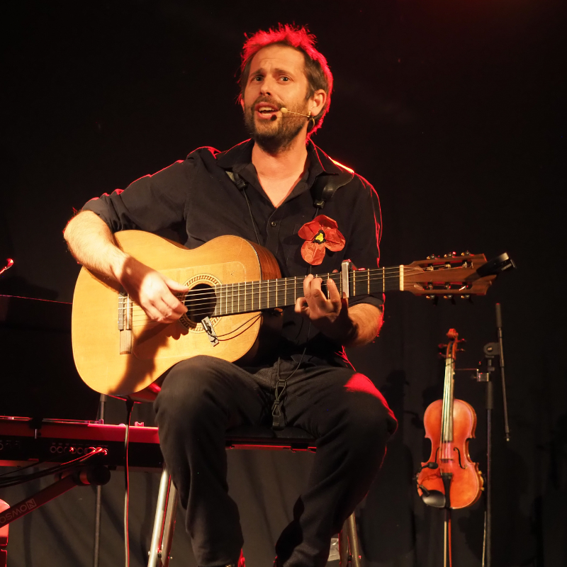 Norbert Gautier joue de la guitare et interprète la chanson "Carcasse" lors du spectacle "Chansons & Coquelicots", hommage à Anne Sylvestre.