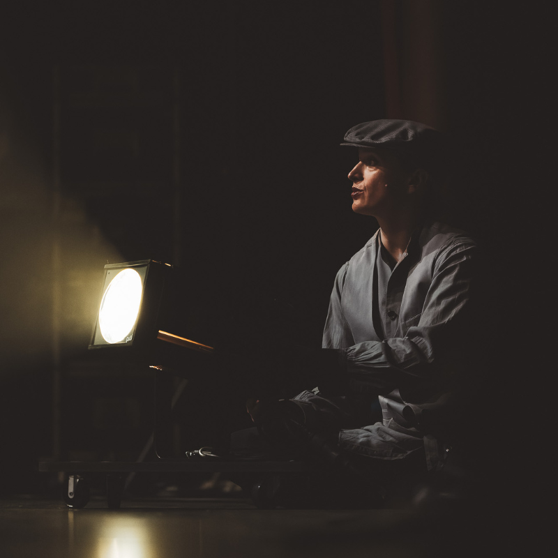 Interprète assis au sol en costume, éclairé par un projecteur dans Splendeur & Décadence