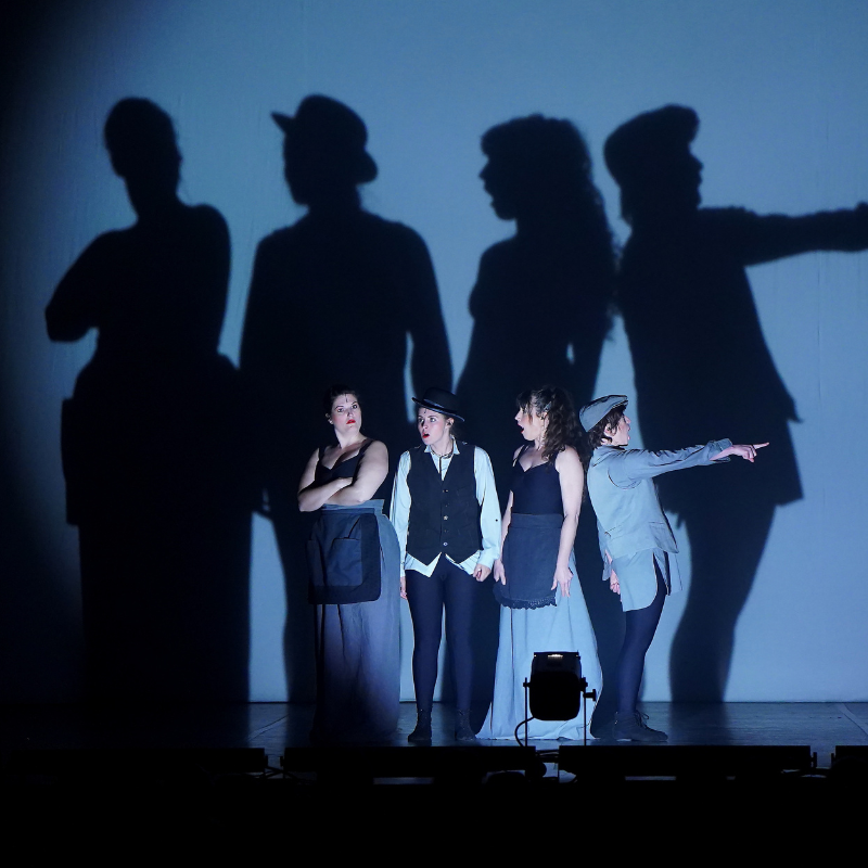 Quatre interprètes en costumes devant un rideau, leurs ombres projetées en grand dans Splendeur & Décadence