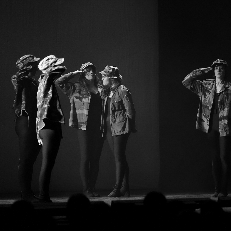 Interprètes en uniformes militaires stylisés, exécutant un salut synchronisé dans Splendeur & Décadence
