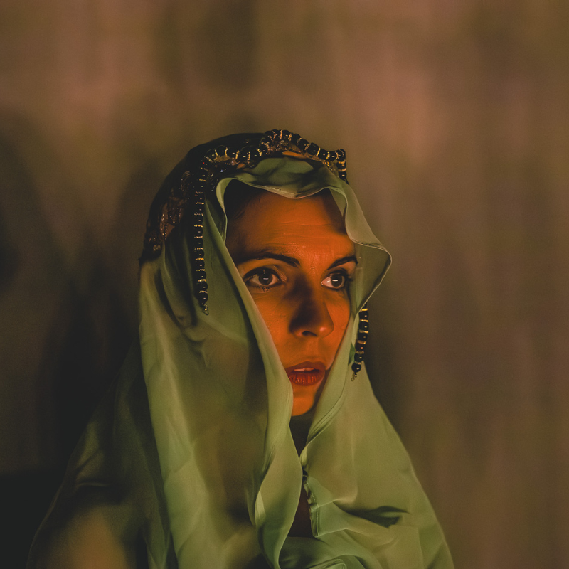 Interprète en drapé vert pâle avec regard intense, éclairée dans Splendeur & Décadence