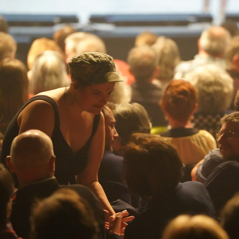 Interprète en tenue militaire stylisée échangeant avec le public dans Splendeur & Décadence