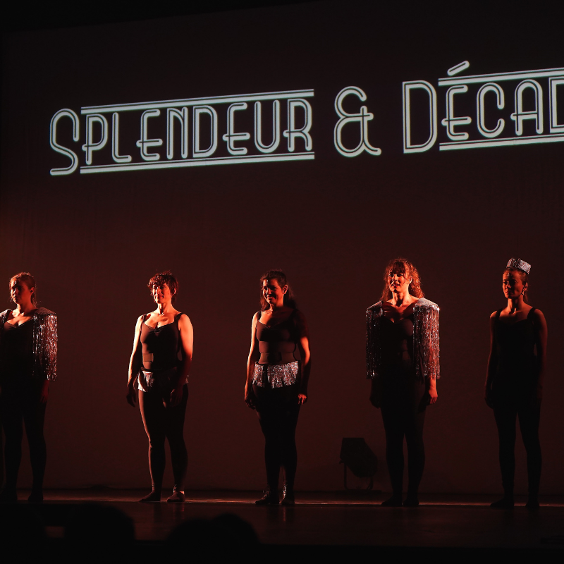 Cinq interprètes alignées sur scène devant le logo lumineux Splendeur & Décadence