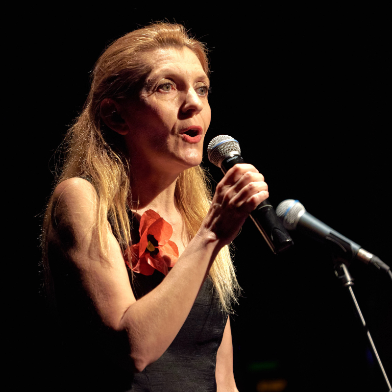 Magali Braconnot interprète une chanson du spectacle Chansons & Coquelicots, hommage à Anne Sylvestre, micro à la main et un coquelicot épinglé sur sa robe.