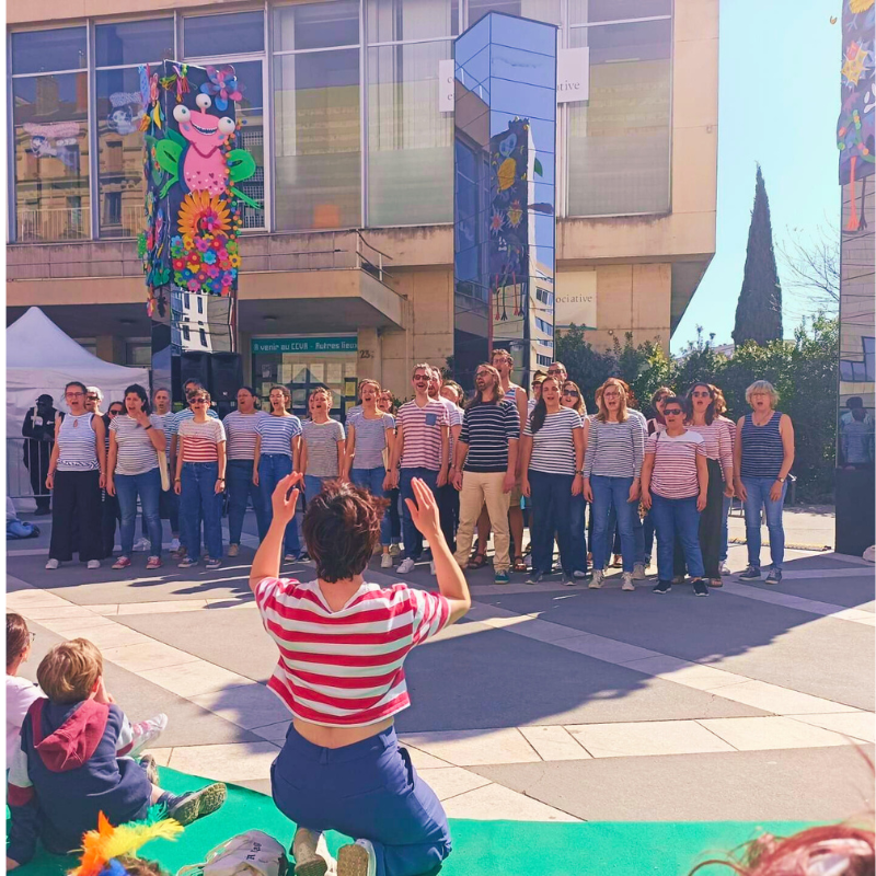 Chorale Pirate interprétant un morceau a cappella en extérieur dirigée face à un public assis